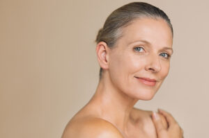 Close-up of an older woman with her hair pulled back, smiling after getting a facelift to restore volume to her face.