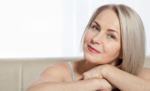 Older woman with her hand stretching her face up to show the results of her facelift.