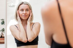Middle-aged woman smiling and touching her face in the mirror after getting a facelift.