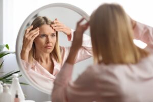 Woman looking at her forehead in the mirror in need of a brow lift for a younger, smoother look.