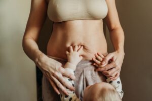 Close-up of a mother with a young child reaching up to her, showing her postpartum body and in need of a mommy makeover.